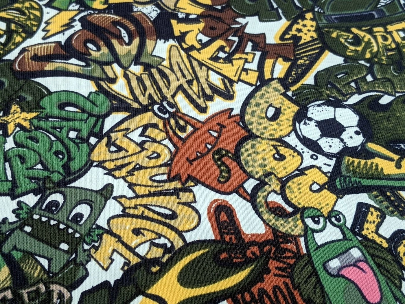 Corileo Stoff »Baumwolljersey Comic Graffiti Kids Fussball Grün Stoff Meterware Jersey«